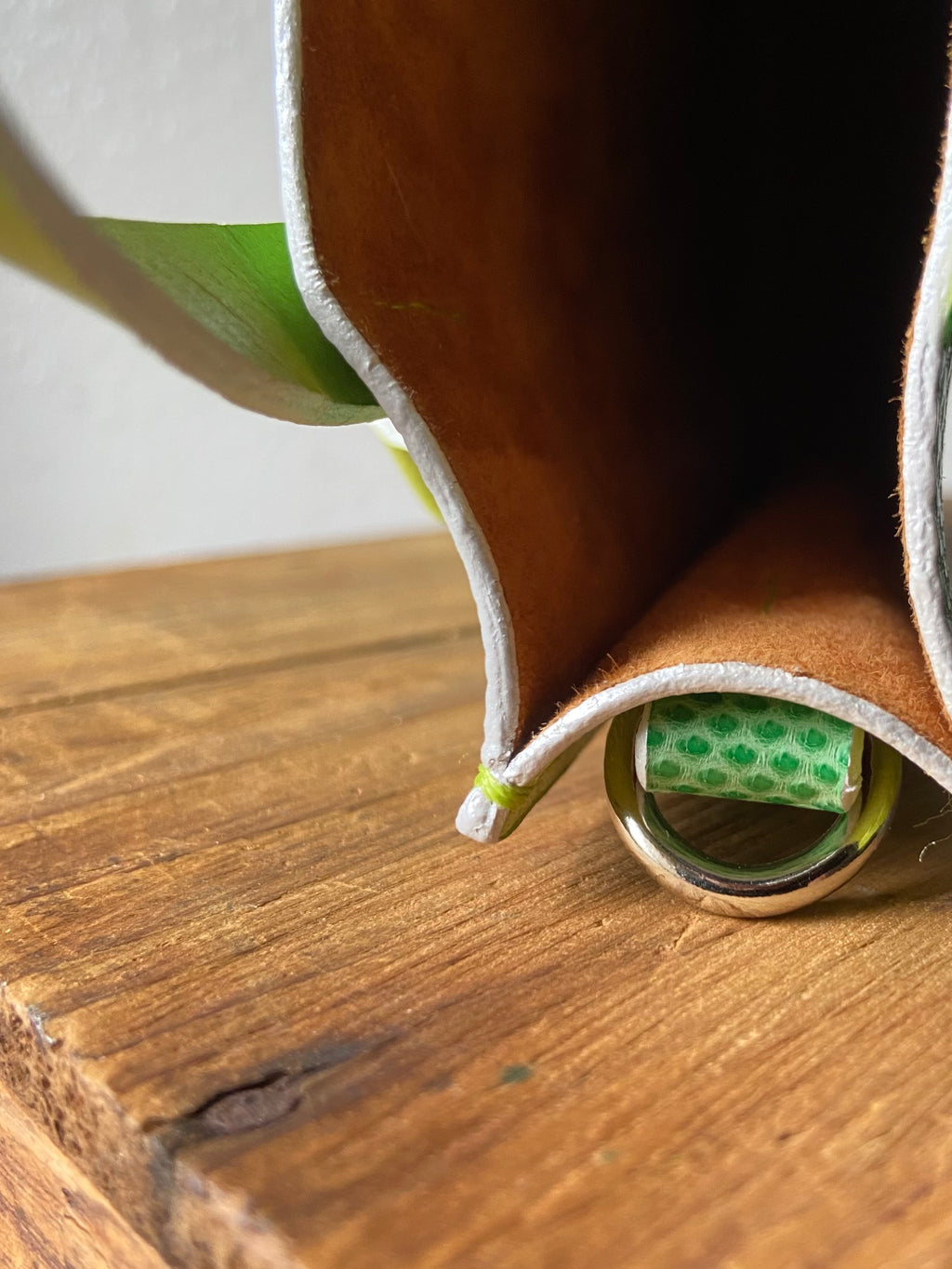 Brown leather wallet with green exterior with brown suede lining on a wooden surface.
