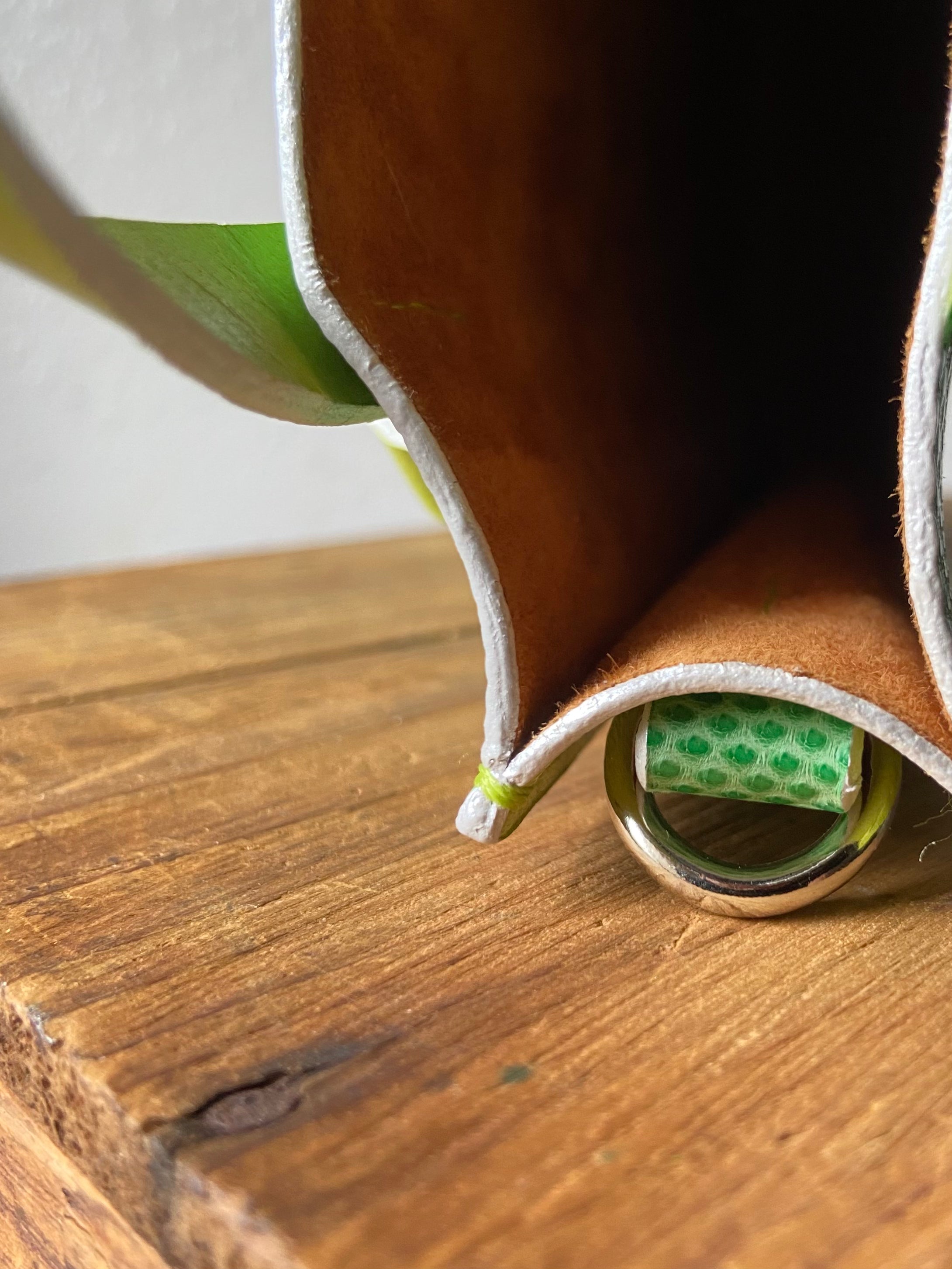 Brown leather wallet with green exterior with brown suede lining on a wooden surface.